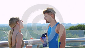 Cheerful Caucasian sporty people speaking and drinking water in city after exercising. Male and female athletes smiling