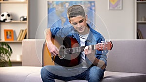 Cheerful Caucasian teenager playing guitar, enjoying favorite hobby, leisure