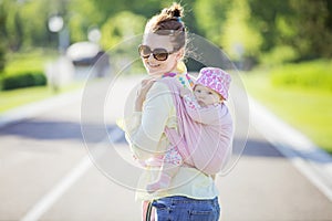 Cheerful Caucasian woman carrying her baby daughter on back outdoors
