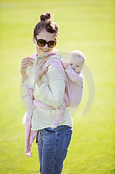 Cheerful Caucasian woman carrying her baby daughter on back in spring park