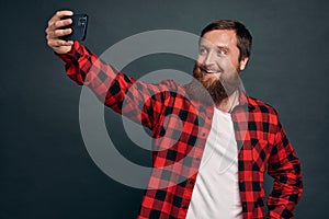 Cheerful and charismatic european guy with beard talking to friend via internet messanger app, holding smartphone raised hand, photo