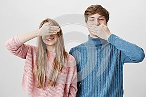 Cheerful charming girl in pink sweater smiles happily with braces and closes eyes, while boy next to her closes mouth