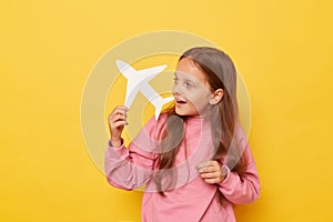 Cheerful charming little girl wearing casual clothing showing airplane and its direction dreaming to traveling having exited