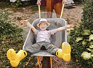 Cheerful child boy laughs in a garden wheelbarrow in the summer