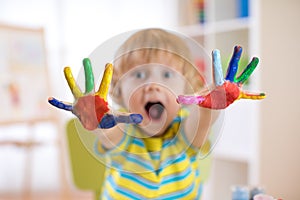 Cheerful child boy showing hands painted in bright colors. Focus on color palms