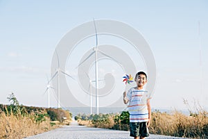 Boy& x27;s playful fascination near wind turbines holding a pinwheel toy