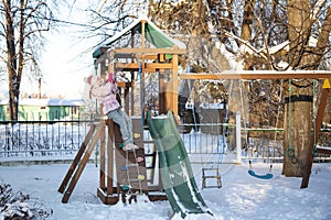 A cheerful child girl plays on the Playground on a snowy winter day