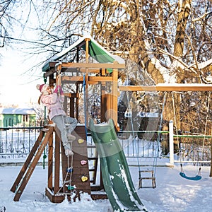 A cheerful child girl plays on the Playground on snowy winter day