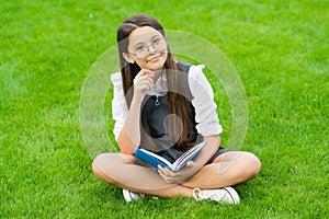 cheerful child in glasses reading book sitting on green grass
