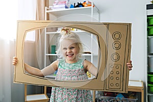 Cheerful child playing with cardboard tv at home. future dream profession concept