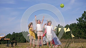 Cheerful childhood, friends boy and girls having fun at childly picnic jump and release balls on forest meadow against