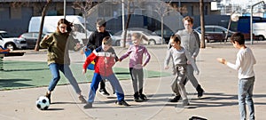 Cheerful children are jogning with ball on the street