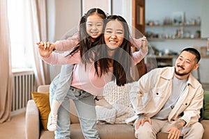 Cheerful Chinese Mom Carrying Baby Daughter Piggyback Playing At Home