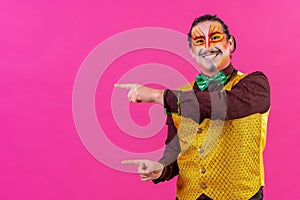 Cheerful circus performer pointing on an empty pink background for copyspace photo