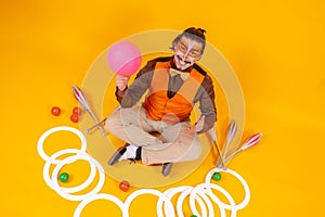 Cheerful circus performer sitting on the ground surrounded by various juggling equipment