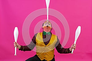 Cheerful circus performer skillfully juggling a number of clubs isolated on pink background