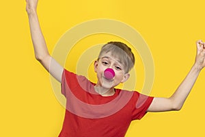 Cheerful clown kid child. April fools day. Child with red clown nose on yellow background