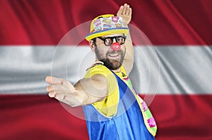 A cheerful clown stands in a welcoming pose against the background of the flag of Austria