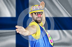 A cheerful clown stands in a welcoming pose against the background of the flag of Finland