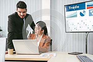 A cheerful and confident Asian businessman stands in the back and points at his businesswoman office colleagues who working.