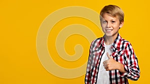 Cheerful confident european teen boy showing thumb up looking at camera, on yellow background