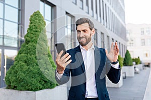 Cheerful confident handsome young caucasian man manager with beard in suit waves hand, have video call