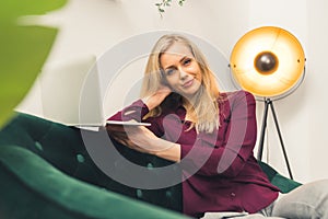 Cheerful confident middle-aged caucasian woman using laptop while sitting on green sofa in her modern living room