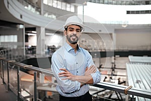 Cheerful confident millennial middle eastern male engineer in protective helmet with beard crossed arms