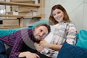 Happy couple in anticipation of a newborn, relaxing together on couch in the home living room. Future loving dad listens to the