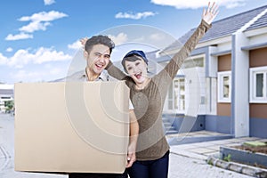 Cheerful couple carrying box at new house