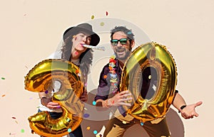 Cheerful couple celebrates a thirty years birthday with big golden balloons