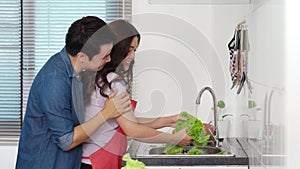 Cheerful couple dancing while washing vegetables in the sink in the kitchen at home. man is hugging woman