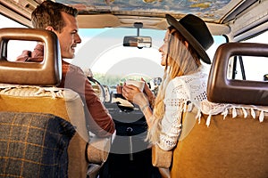 Cheerful couple enjoying a road trip. Smiling man and woman talking while driving retro van