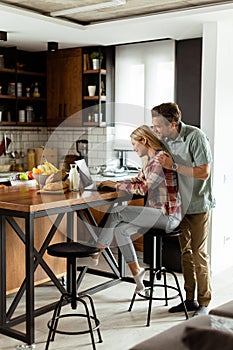 Cheerful couple enjoys a light-hearted moment in their sunny kitchen, working on laptop surrounded by a healthy breakfast