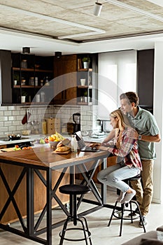 Cheerful couple enjoys a light-hearted moment in their sunny kitchen, working on laptop surrounded by a healthy breakfast