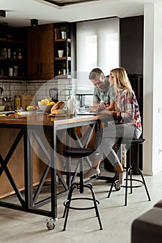 Cheerful couple enjoys a light-hearted moment in their sunny kitchen, working on laptop surrounded by a healthy breakfast