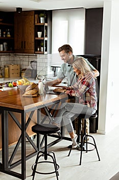 Cheerful couple enjoys a light-hearted moment in their sunny kitchen, working on laptop surrounded by a healthy breakfast