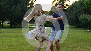Cheerful couple having fun in green park holding hands and spinning looking at each other. Young Caucasian man and woman