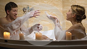 Cheerful couple having fun playing with water and foam in whirlpool, romance