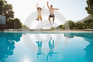 Cheerful couple jumping into swimming pool