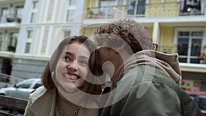 Cheerful couple laughing on city street. Man whispering funny story to woman.