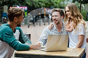 Cheerful couple looking at friend while sitting at sidewalk cafe