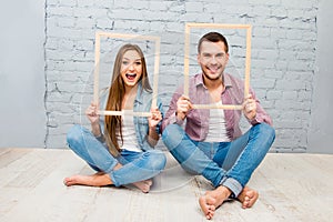 Cheerful couple in love sitting on the floor and holding wooden frames