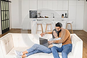 Cheerful couple in love spending leisure time online with a laptop at home. Young woman and man looking at the laptop