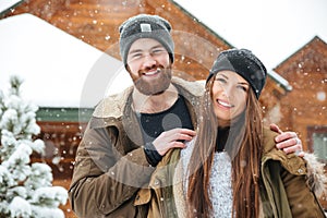 Cheerful couple near wooden cottage in winter
