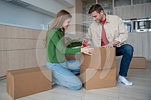 Cheerful couple packing cardboard boxes using sticky tape prepare to move in new apartment together.