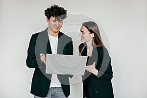 Cheerful couple posing with modern laptop and wearing elegant black blazers and accessories for men and women, white