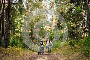 Cheerful couple pushing bicycles and walking along the forest road. Happy couple with bicycle walking through park and talking and