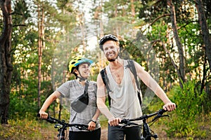 Cheerful couple pushing bicycles and walking along the forest road. Happy couple with bicycle walking through park and talking and