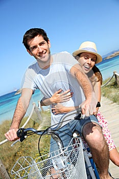 Cheerful couple riding bike by the seaside